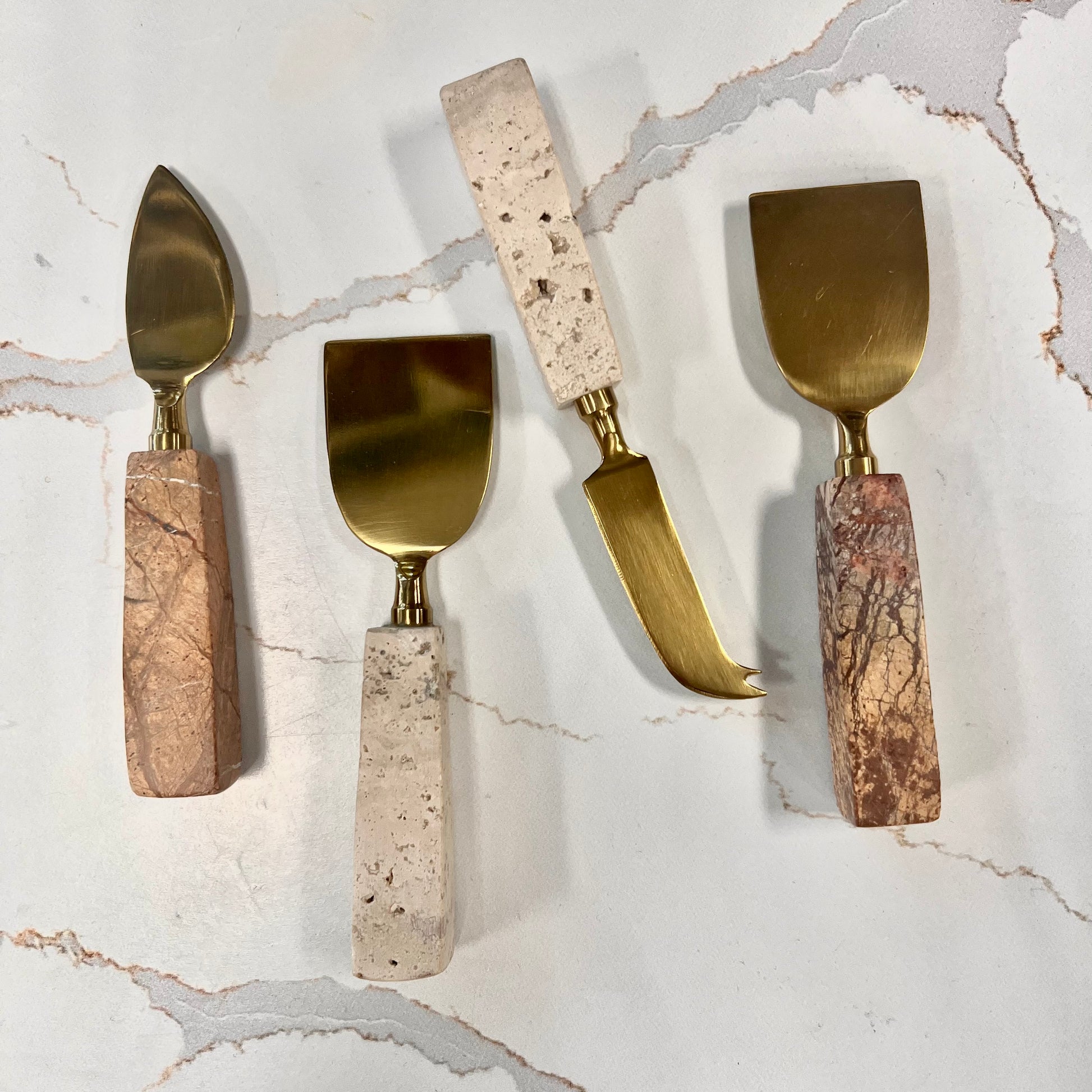 4 styles of travertine cheese utensil arranged on a marble background.