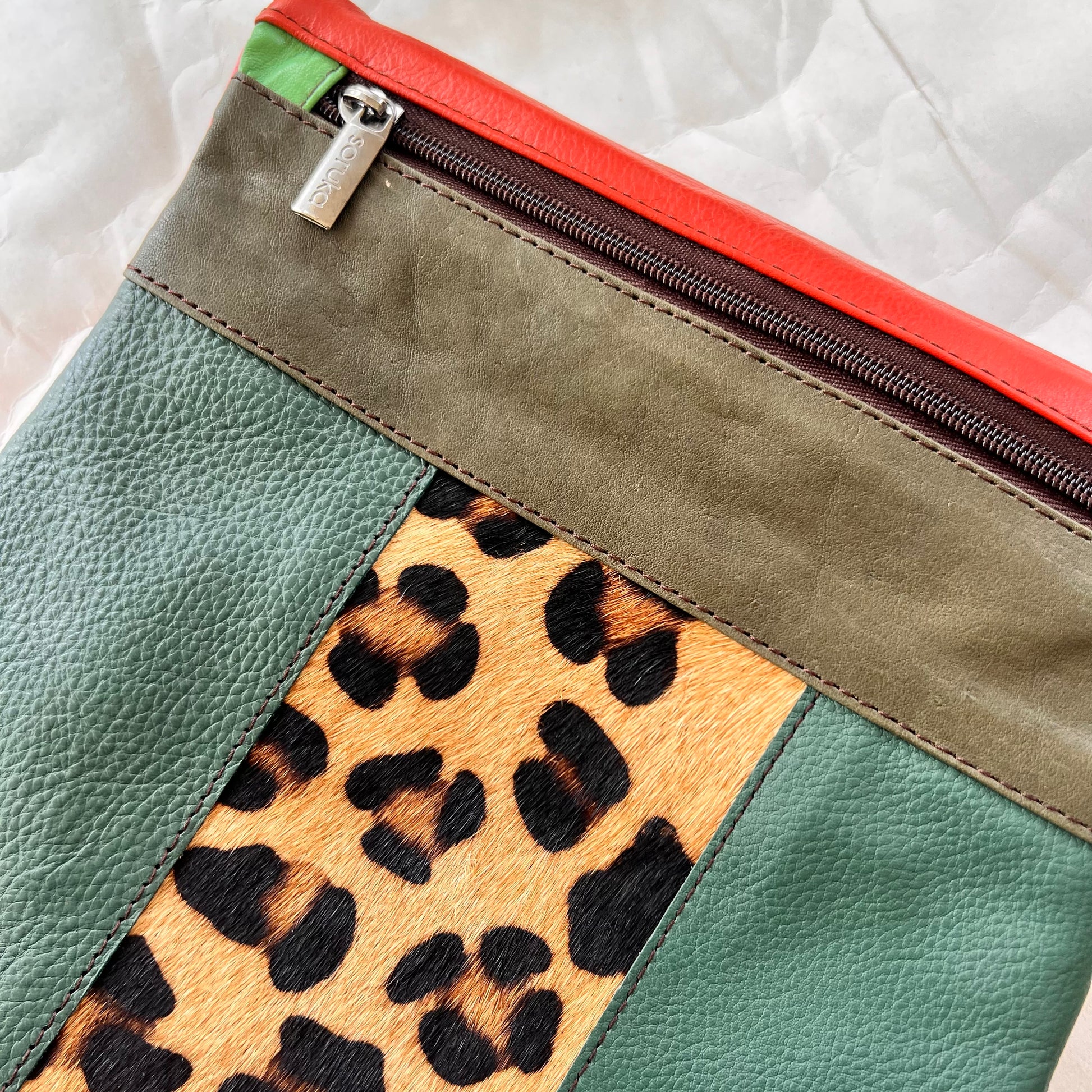 close-up of green greta bag with animal print block in the center with olive stripe and zipper across the top.