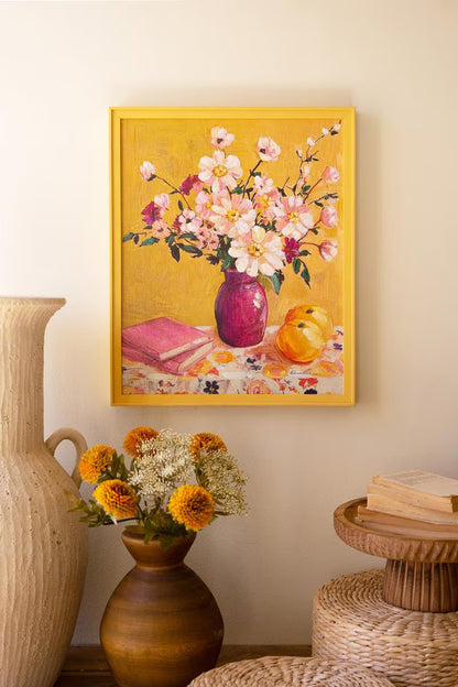 Framed floral painting on a wall with decorative vases and books below.