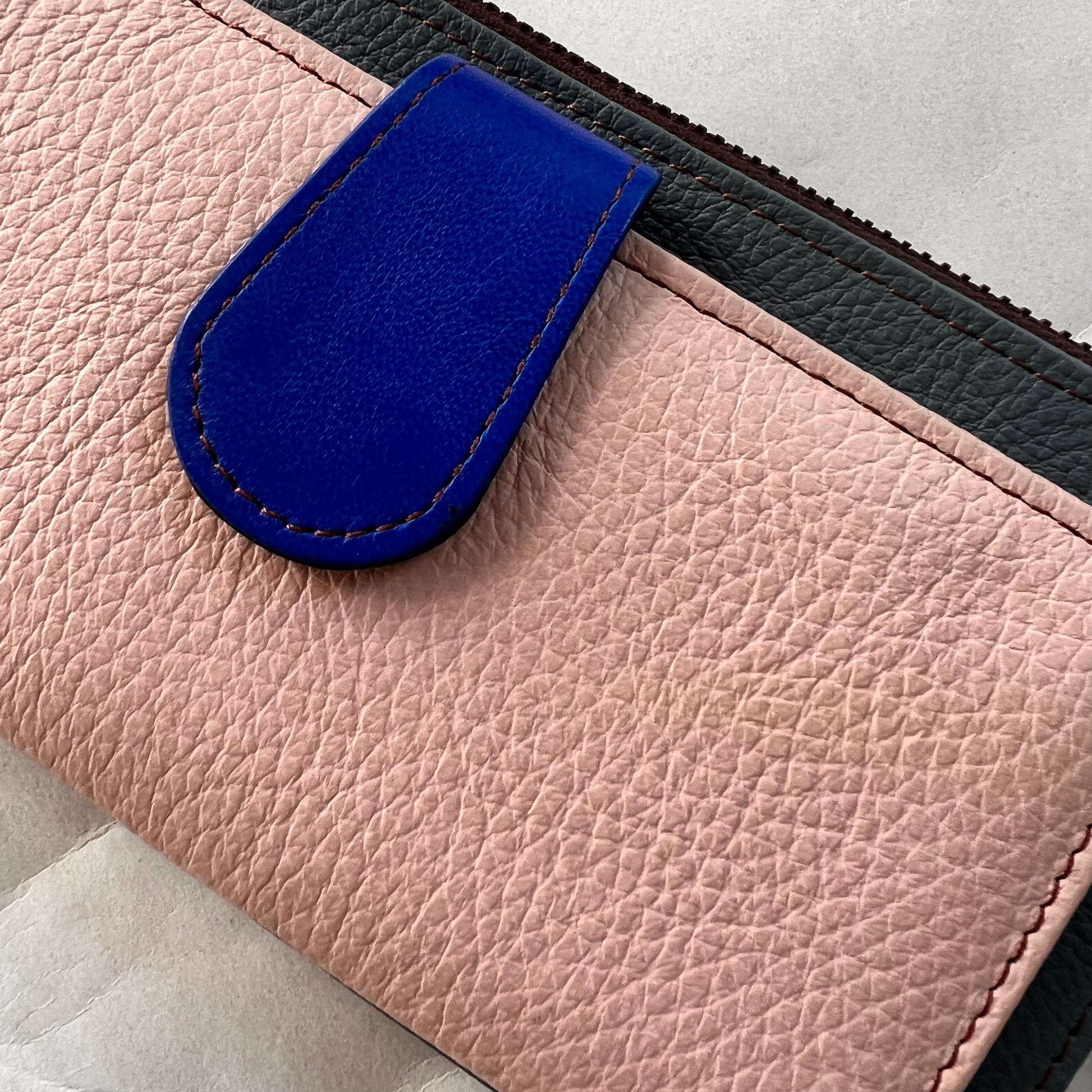 close-up of rectanglar kimber teal wallet with pink pocket and blue tab closure.