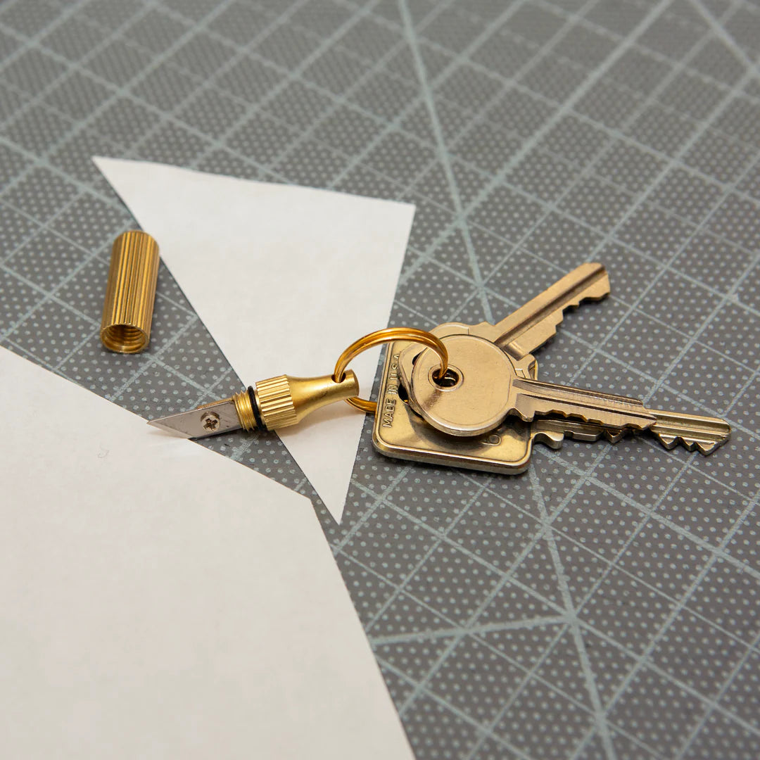 Mini Knife Keychain with keys on the ring laying on a desk with a cut piece of paper.