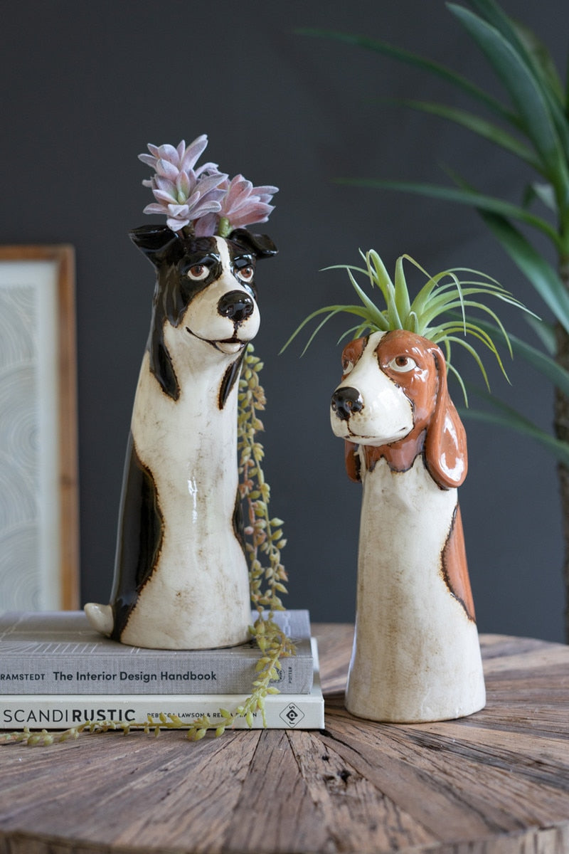 One brown and one black dog planter with succulents in them, set on a table with books.