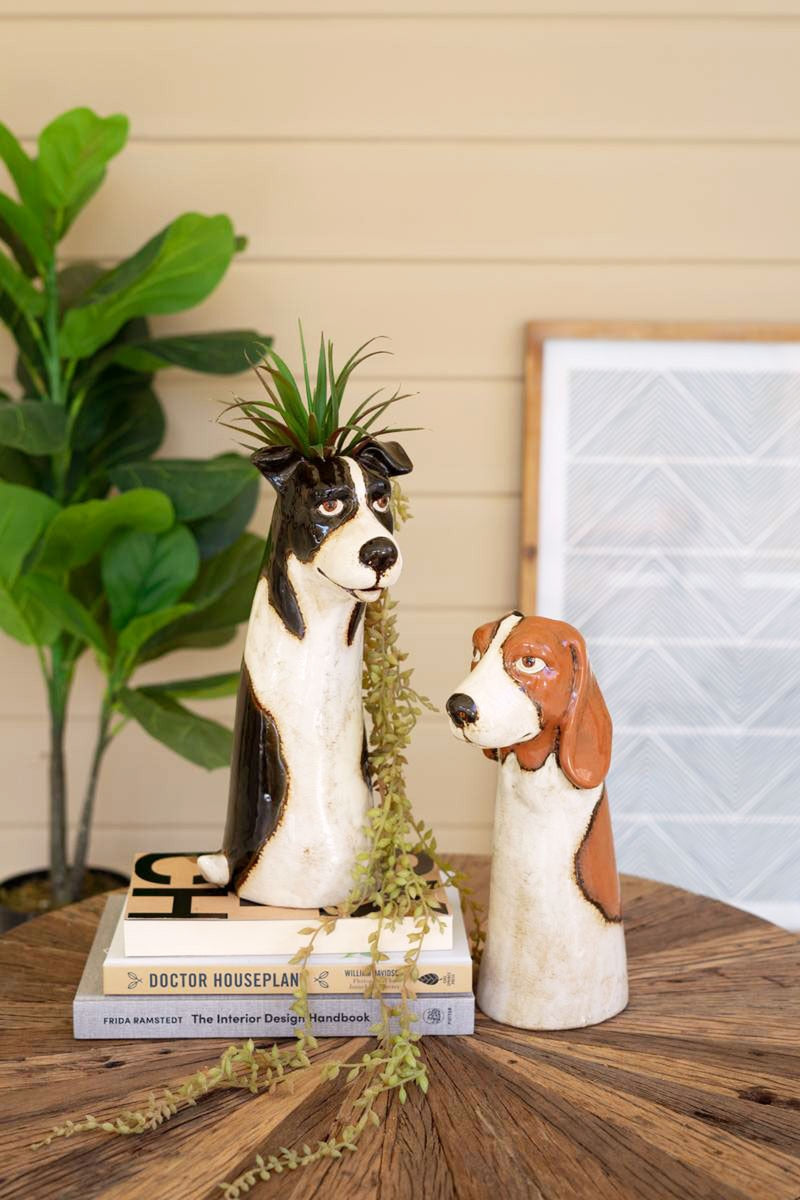 Two styles of dog planters set on a table with books, one planter has succulents in it.