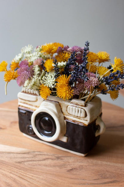 Angled top view of black and white camera planter filled with colorful flowers.