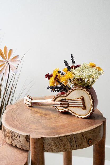 Ceramic guitar planter filled with flowers and set on a wooden table.