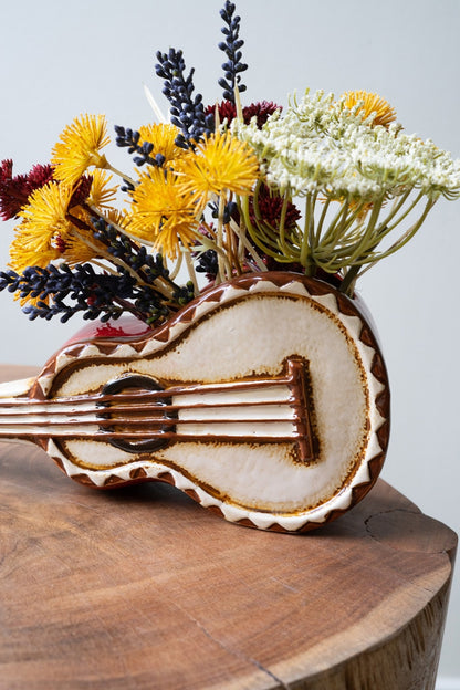 Close up of ceramic guitar planter filled with flowers.