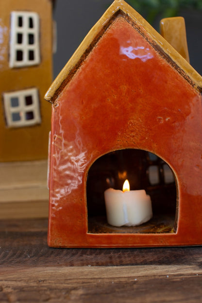 Back view of small red wonky house with lit tea light in it.