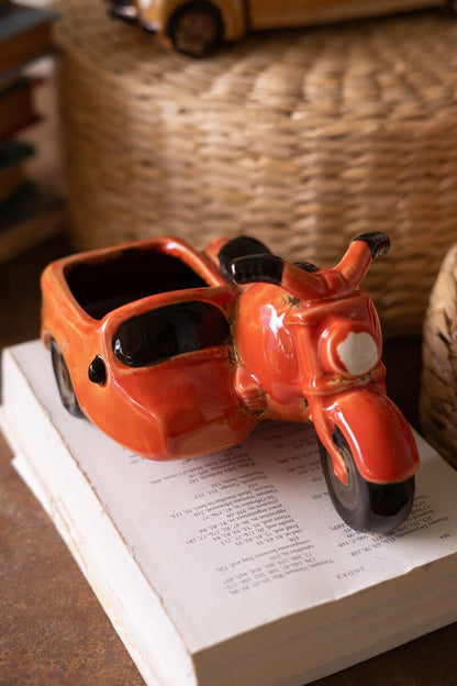 orange Ceramic Motorcycle With Sidecar Planter without flowers set on a book
