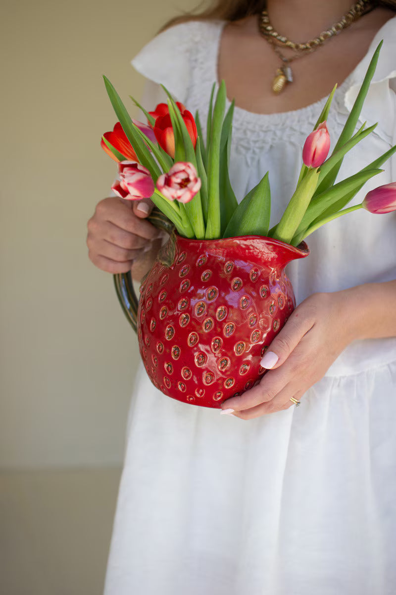 Person holding a red strawberry pitcher filled with tulips against a neutral background