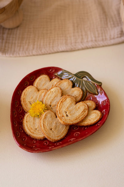 red Ceramic Strawberry shaped Platter with green leaves painted on top filled with cookies.