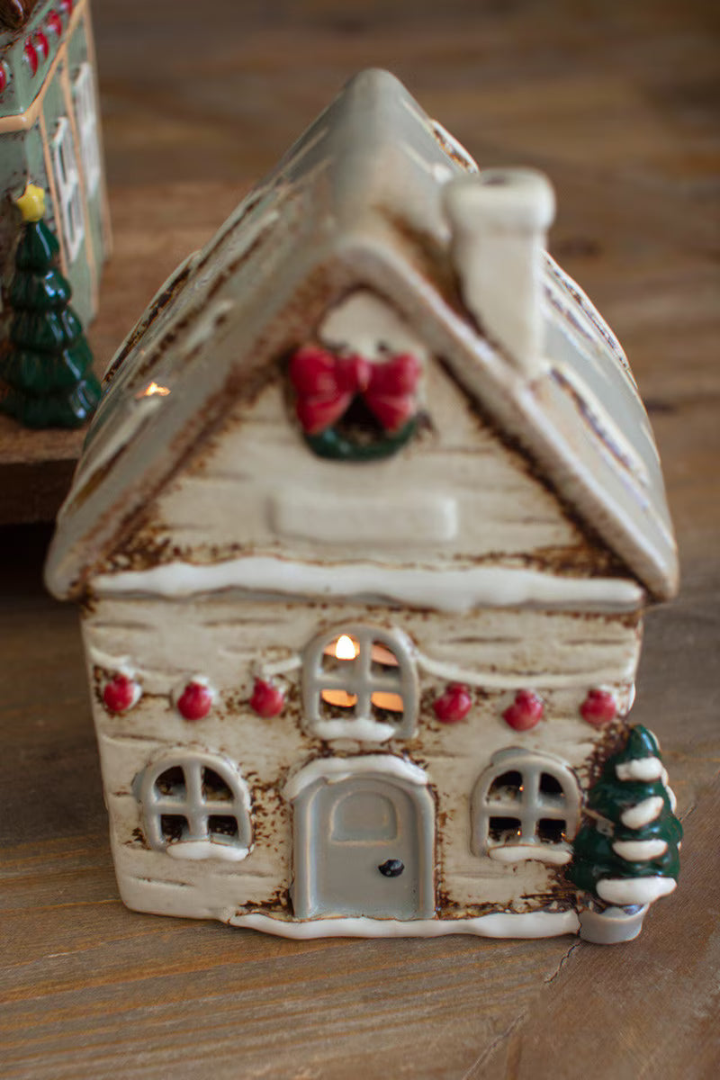 Decorative ceramic house with a wreath and small tree on a wooden surface