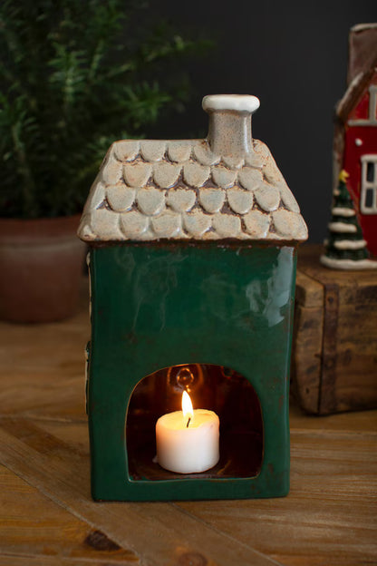 back view of Green ceramic house with a lit candle inside on a wooden surface.