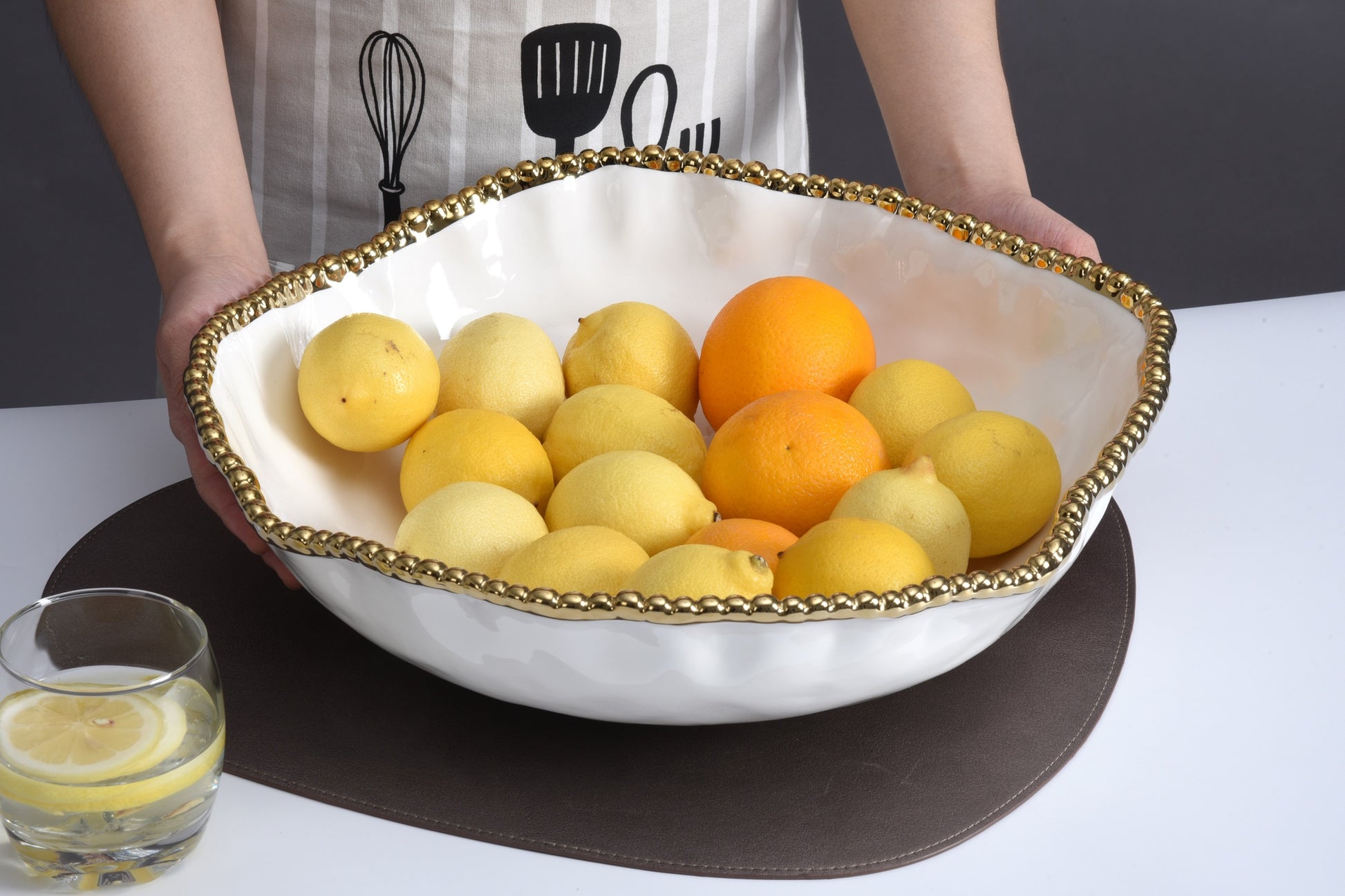 hands holding white bowl with gold beaded rim filled with fruit