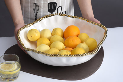 hands holding white bowl with gold beaded rim filled with fruit