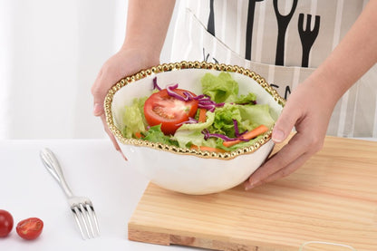 hands holding white serving bowl with gold beaded rim filled with salad