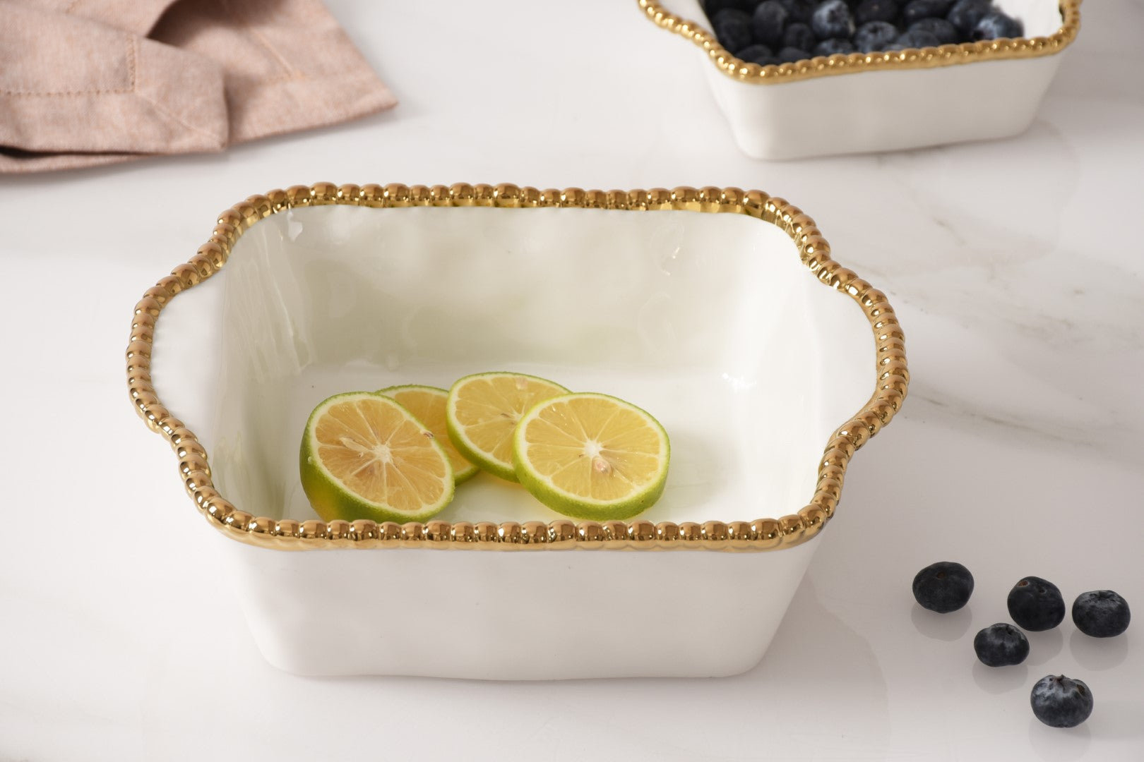 white Baking Dish with gold beaded rim with fruit in it
