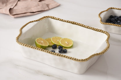 white baking dish with gold rim set on a marble surface with fruit in it