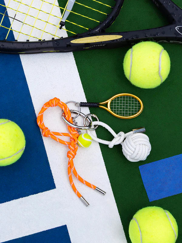 tennis bag charm laying on a green and blue background with tennis balls