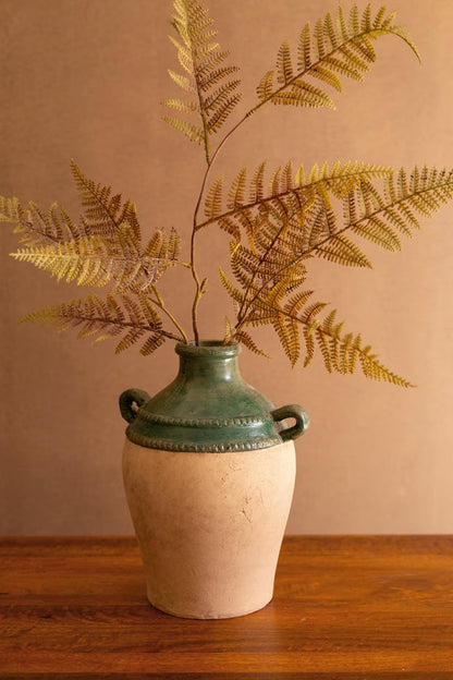 Ceramic vase with green top and natural base, containing dried fern leaves on a wooden surface.