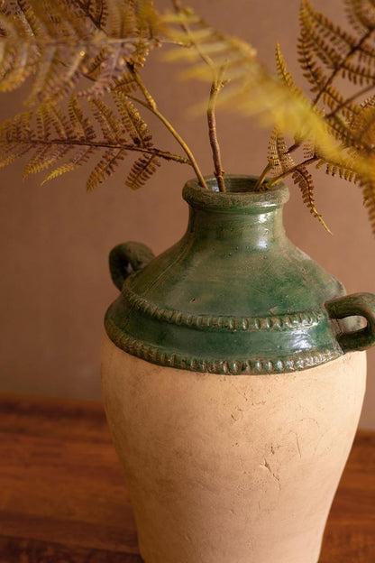 Green ceramic vase with handles and a textured surface, containing dried ferns against a neutral background.