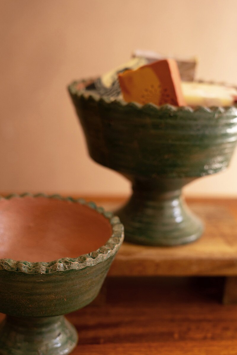 Two green ceramic footed bowls with textured rims on a wooden surface.