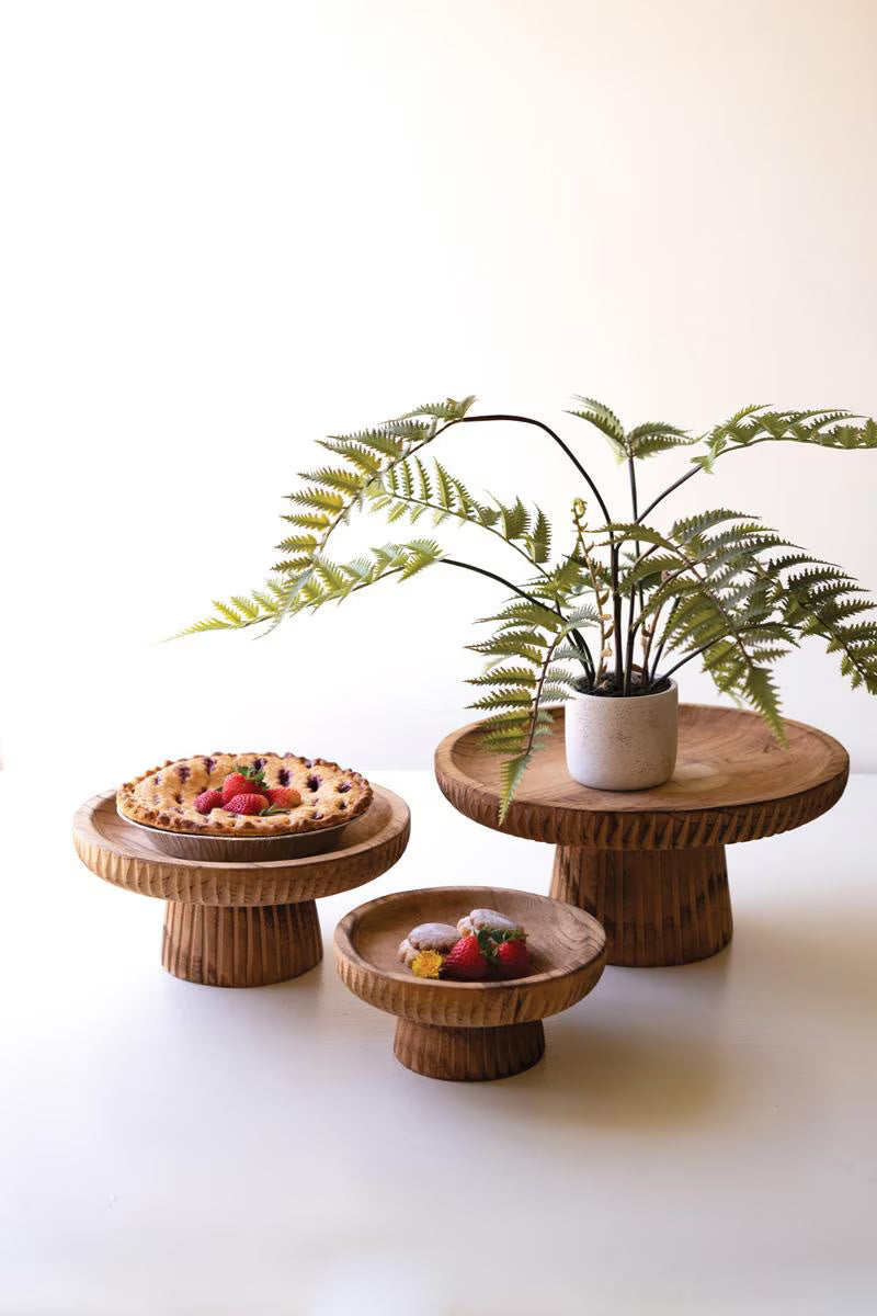 3 sizes of Wooden cake stands with a plant and small desserts on a white background