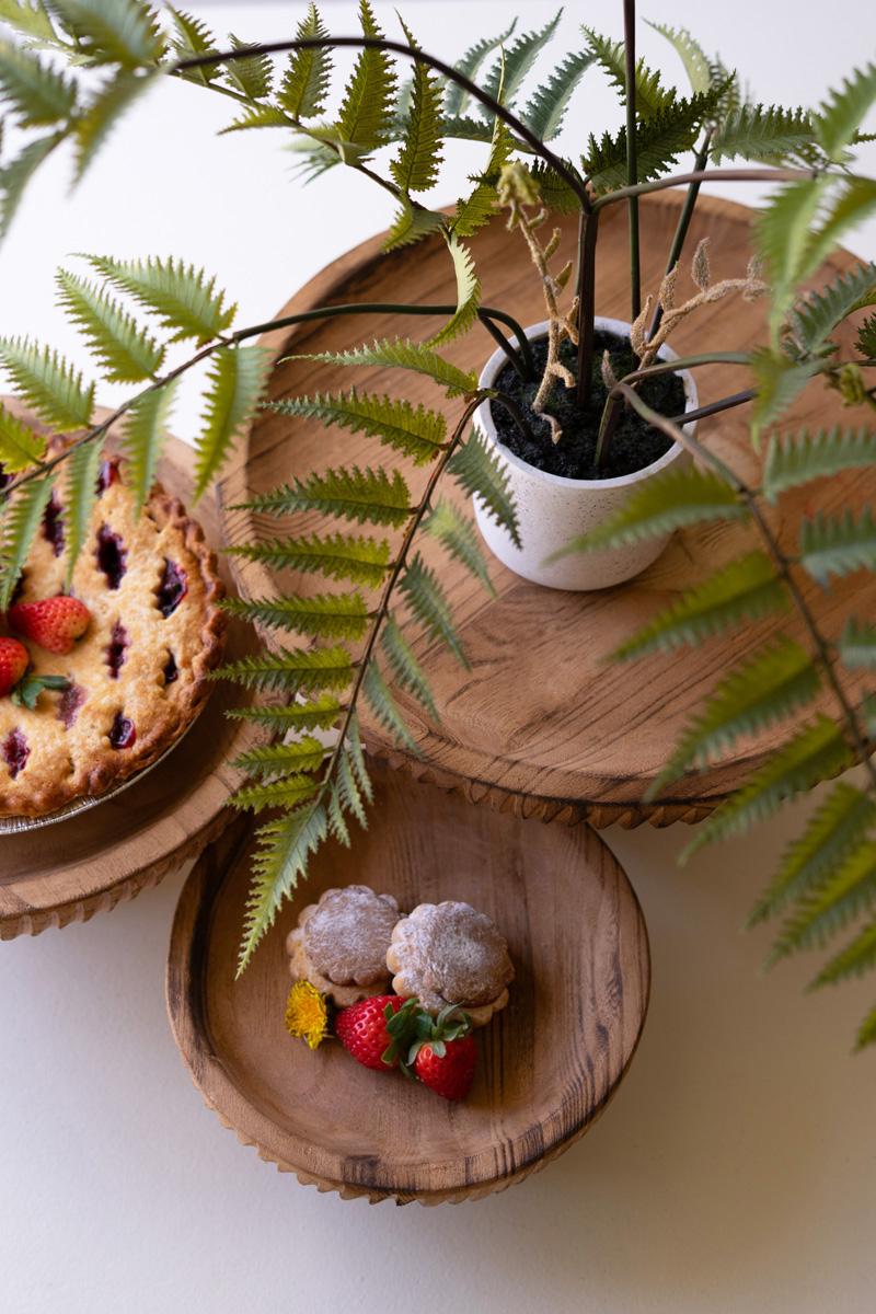 top view of Wooden plates with desserts and a pie, surrounded by green fern leaves.