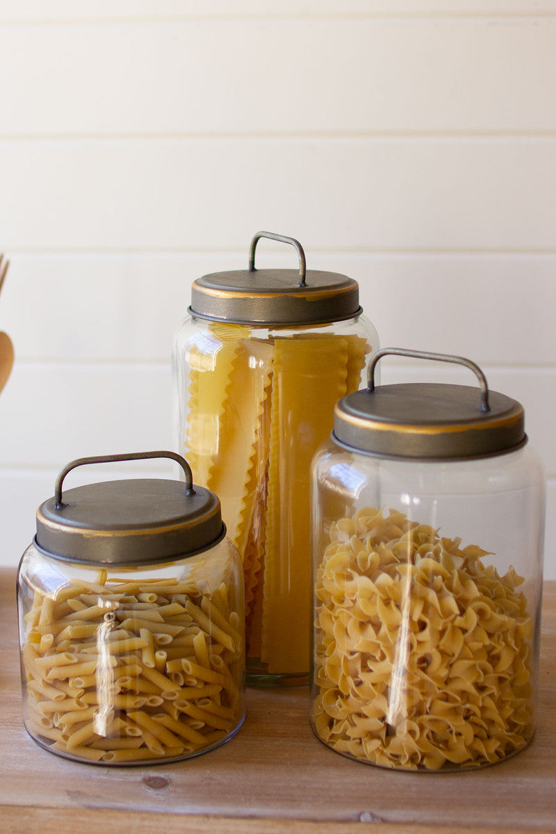 3 sizes glass canisters filled with pastas and set on a wooden countertop.