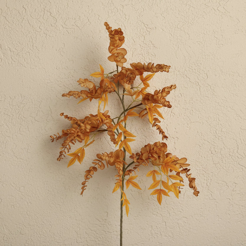 An artificial autumn ornamental grass stem with textured orange and yellow leaves on a beige background.