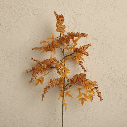 An artificial autumn ornamental grass stem with textured orange and yellow leaves on a beige background.