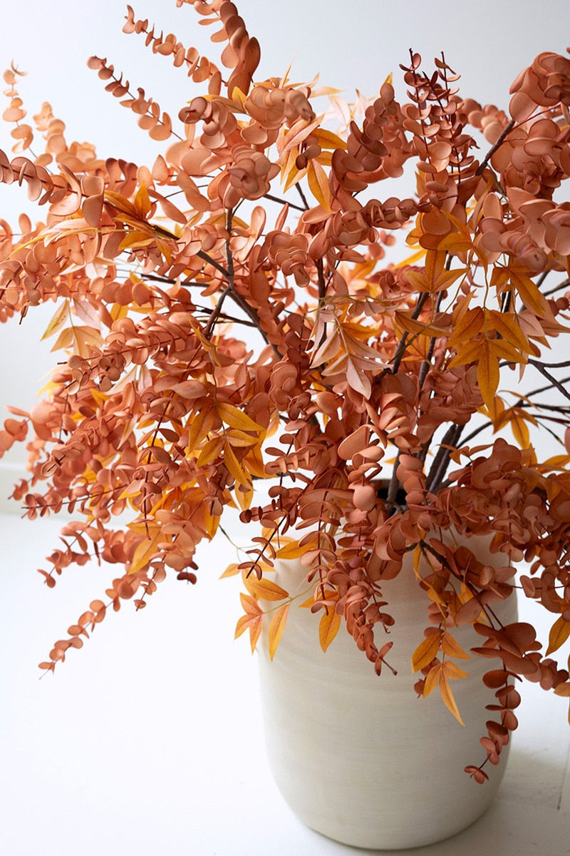 Artificial orange foliage in a white vase on a white background