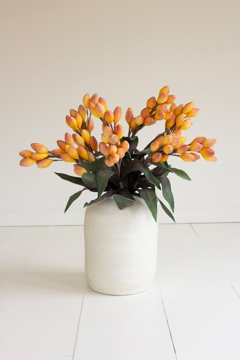 White vase with yellow and green artificial flowers on a light background