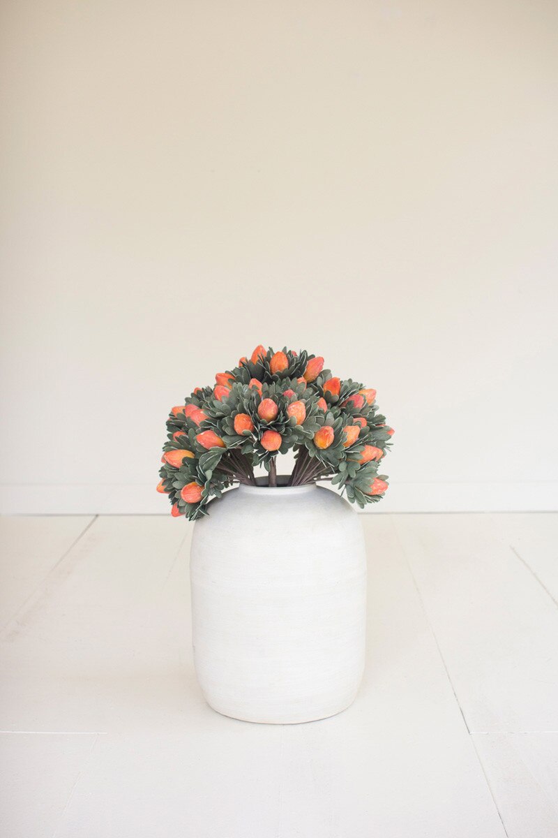 greenery stems with orange pods in them in a large white vase on an off-white background