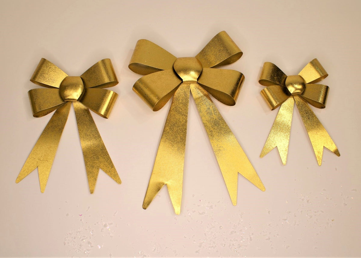 three gold metal bows of different sizes on a tan background