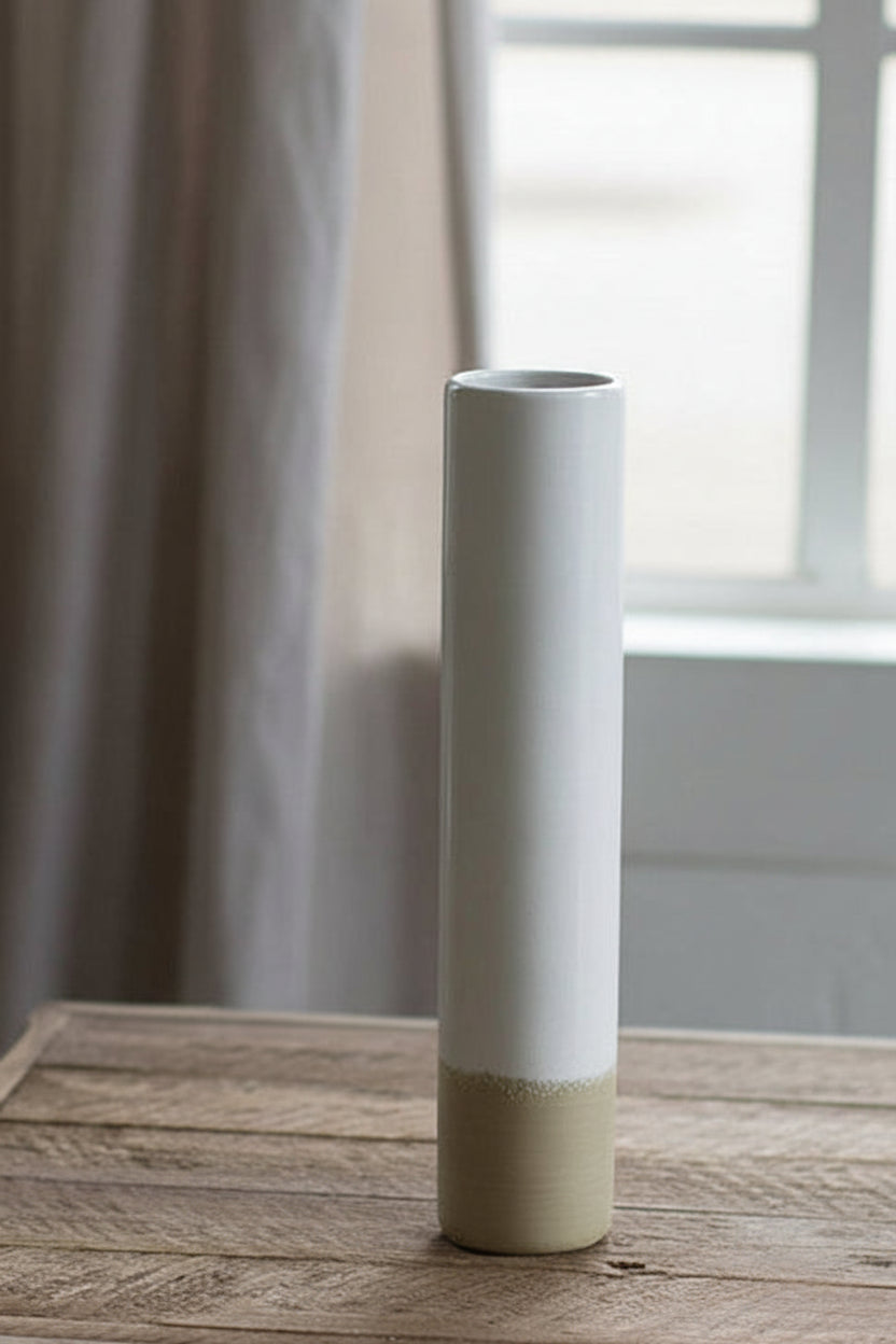 tall Ceramic Cylinder Bud Vase set on a wooden table with window and curtains in the background