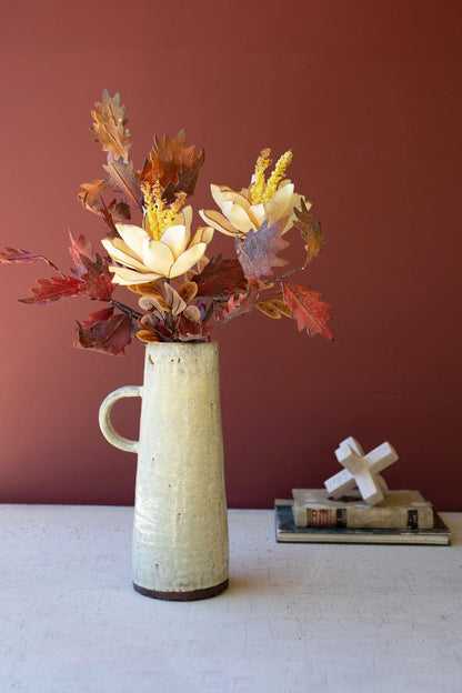 tall pitcher vase filled with botanicals set on a table with books