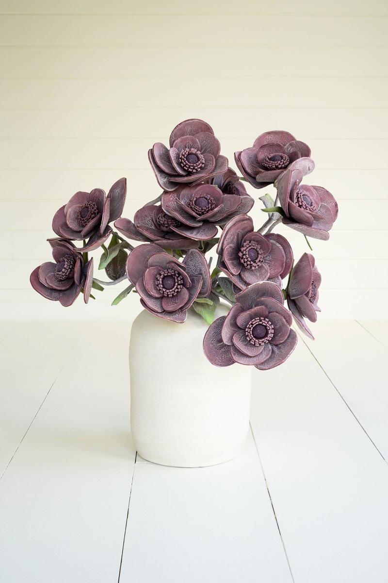 off-white vase filled with plum colored artificial flowers.