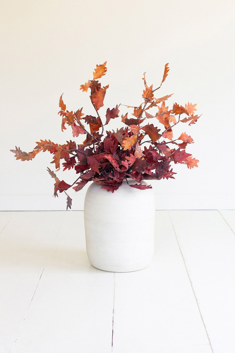 White vase with red and orange leaves on a white floor and wall