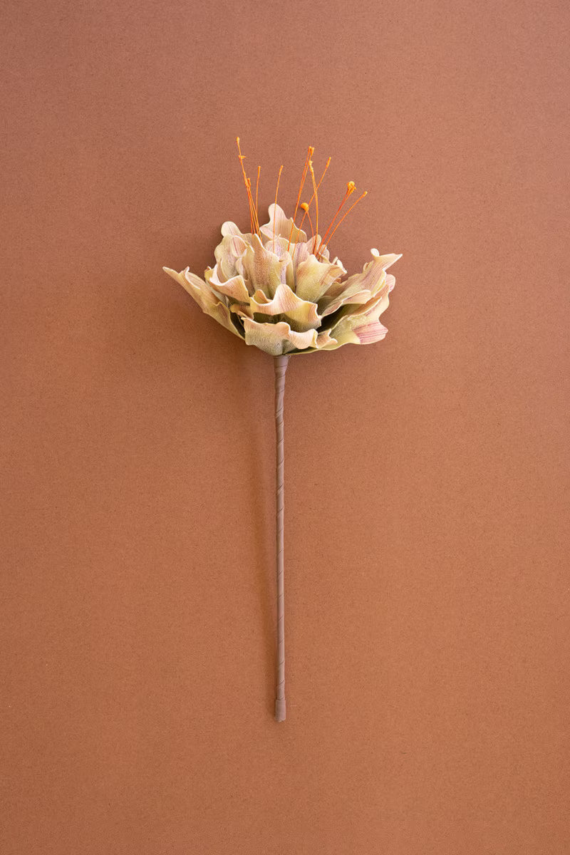 A single artificial flower stem with pale beige petals and orange-tan stamens, centered against a solid warm brown background.