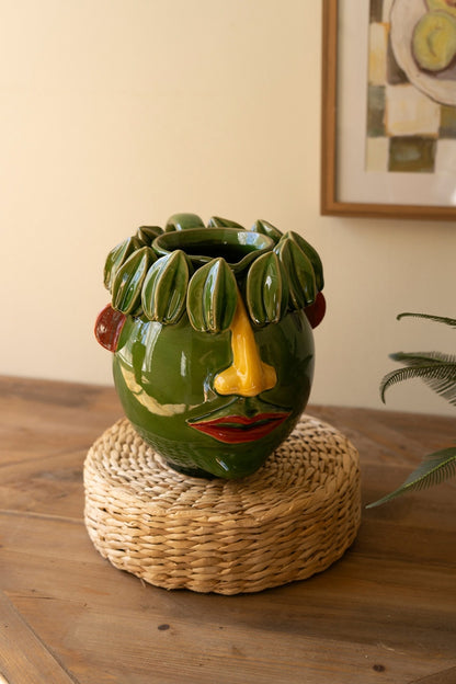 A ceramic head planter with starfruit green design, featuring facial characteristics, placed on a woven mat.