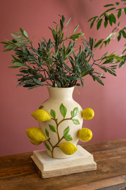 lemon vase filled with olive branches set on a book on  wooden table