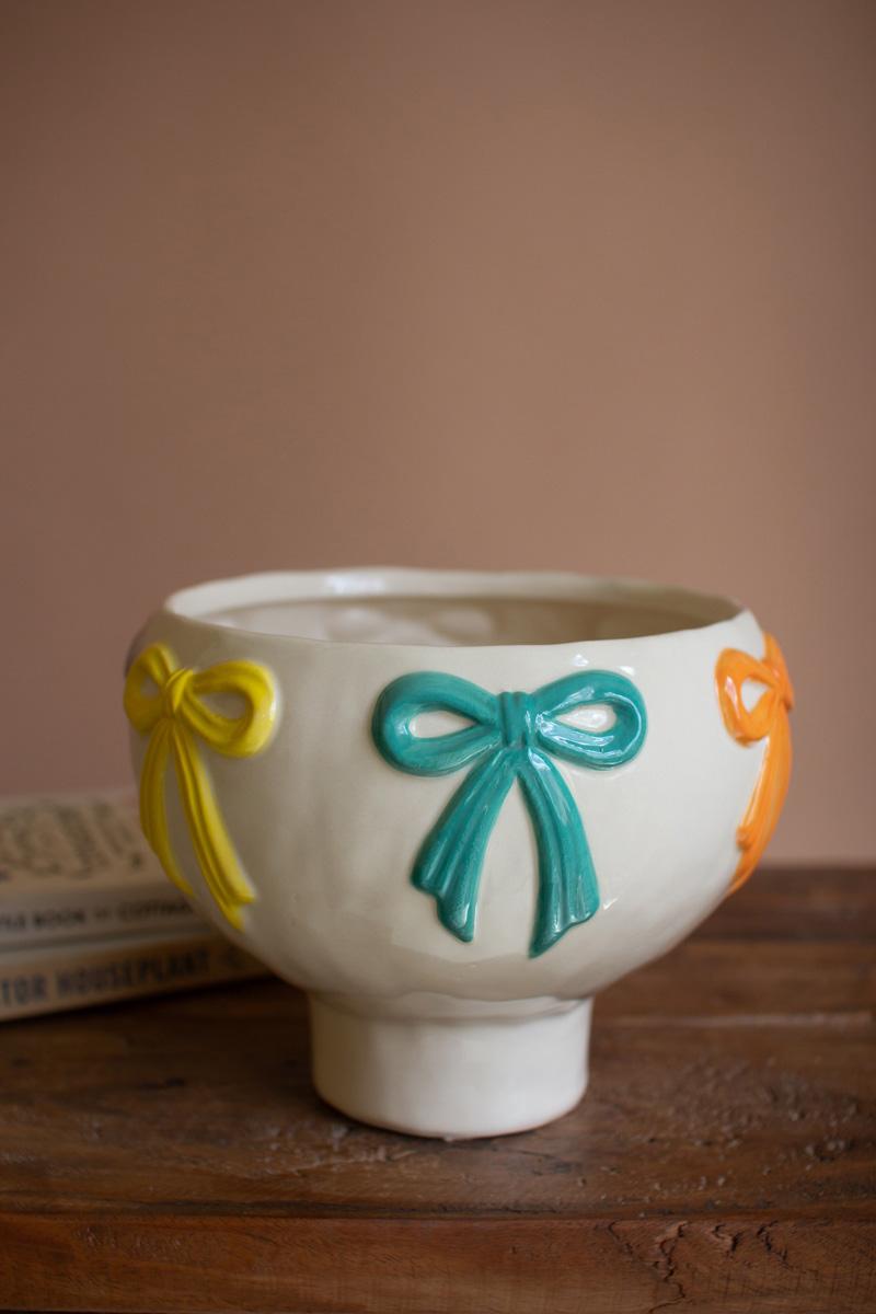 side of white pedestaled bowl with orange, teal and yellow bows around the rim