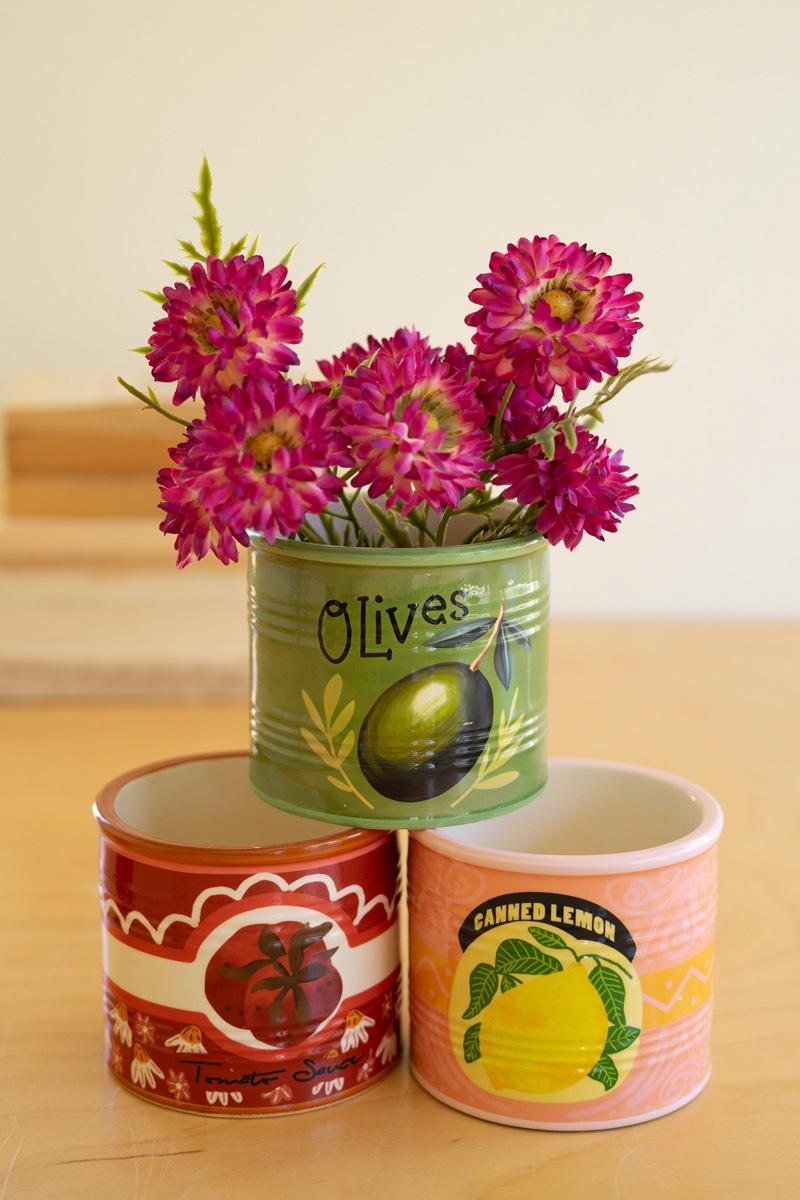 Three decorative ceramic vessels, one with a with floral arrangement in it on a wooden surface