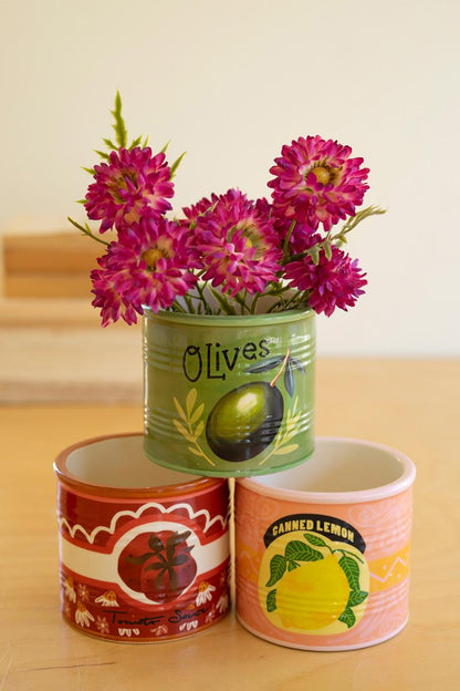 Three decorative ceramic vessels, one with a with floral arrangement in it on a wooden surface