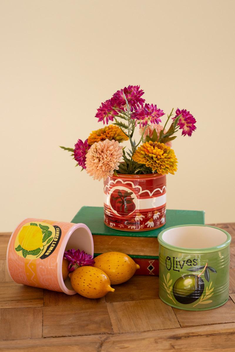 Decorative planters designed as can goods with flowers and lemons on a wooden surface