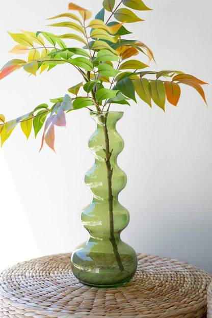 green bubble vase with leafy greenery in it set on a wicker table.