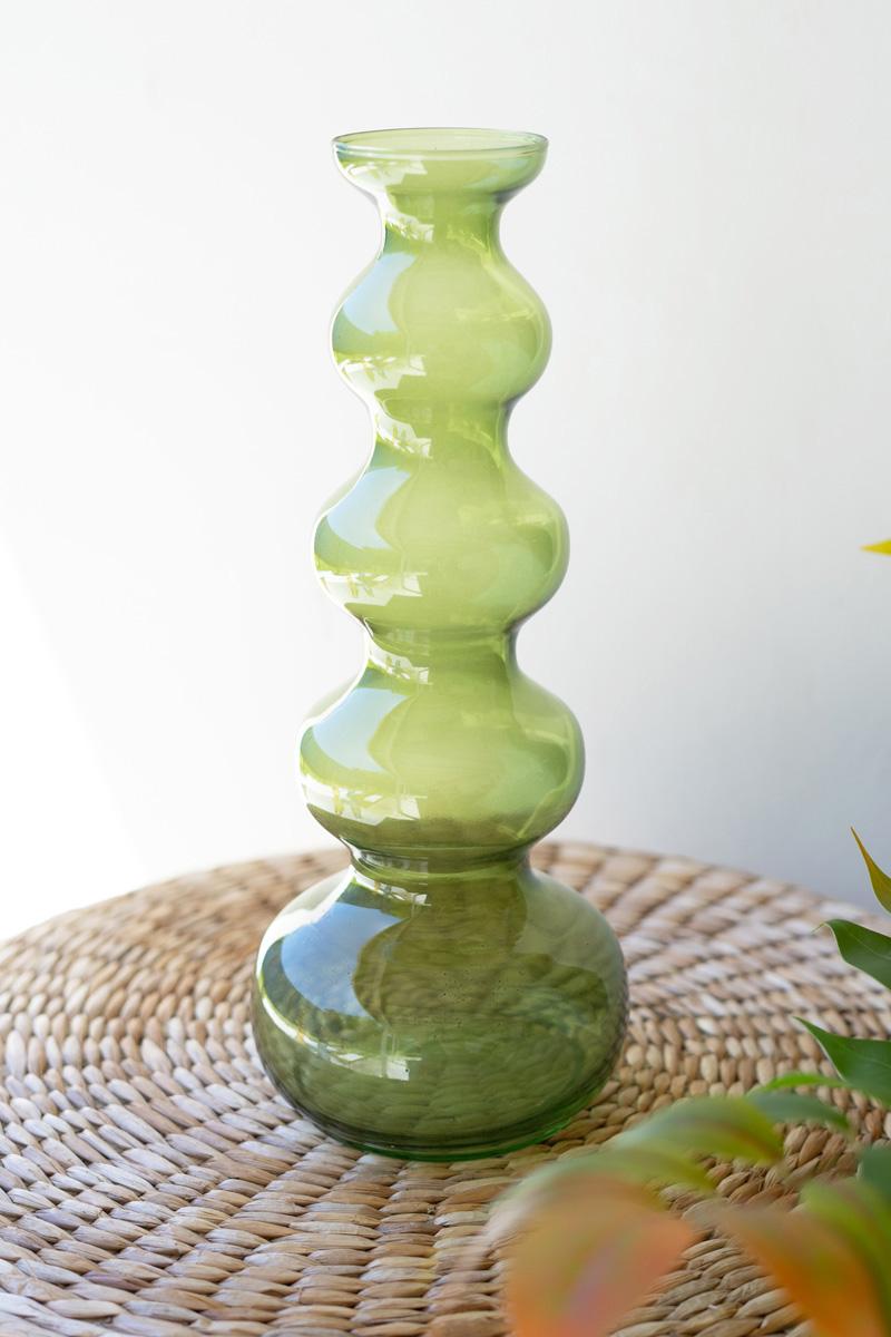 green bubble vase without greenery set on a wicker table.