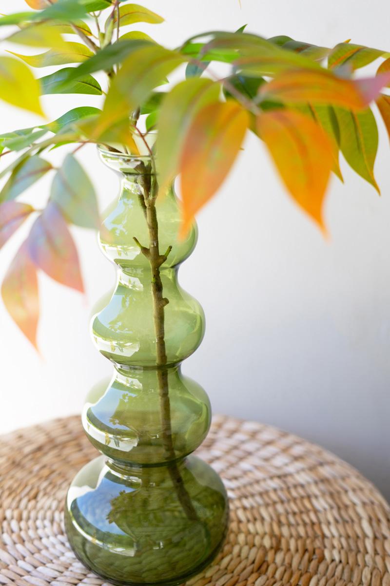 close-up of green glass buble vase with greenery in it.