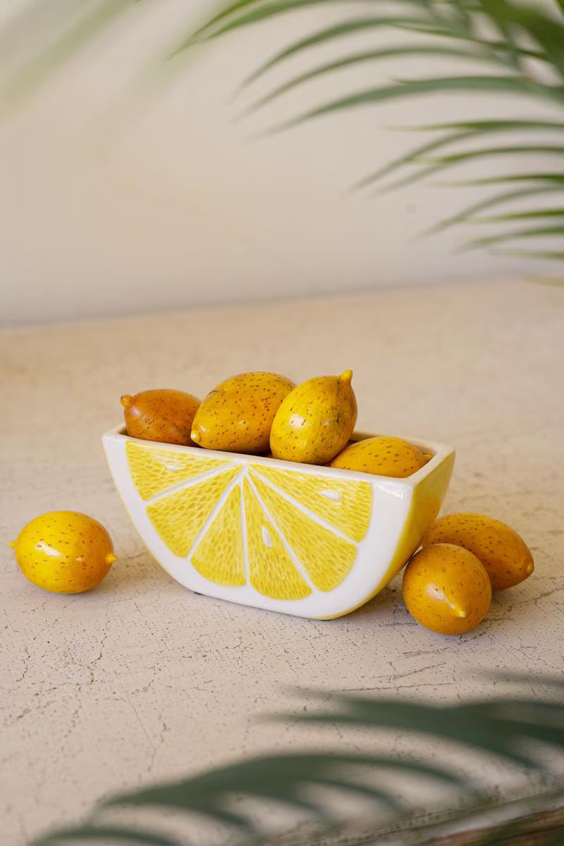vessel in he shape of and painted as a lemon wedge set on a counter and filled with lemons