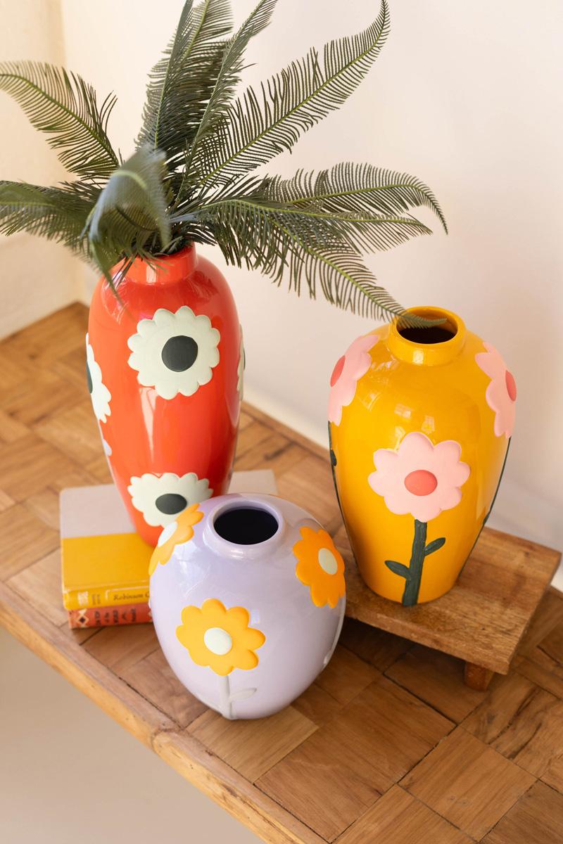 side view of Three colorful vases with floral designs, largest vase has fern fronds in it